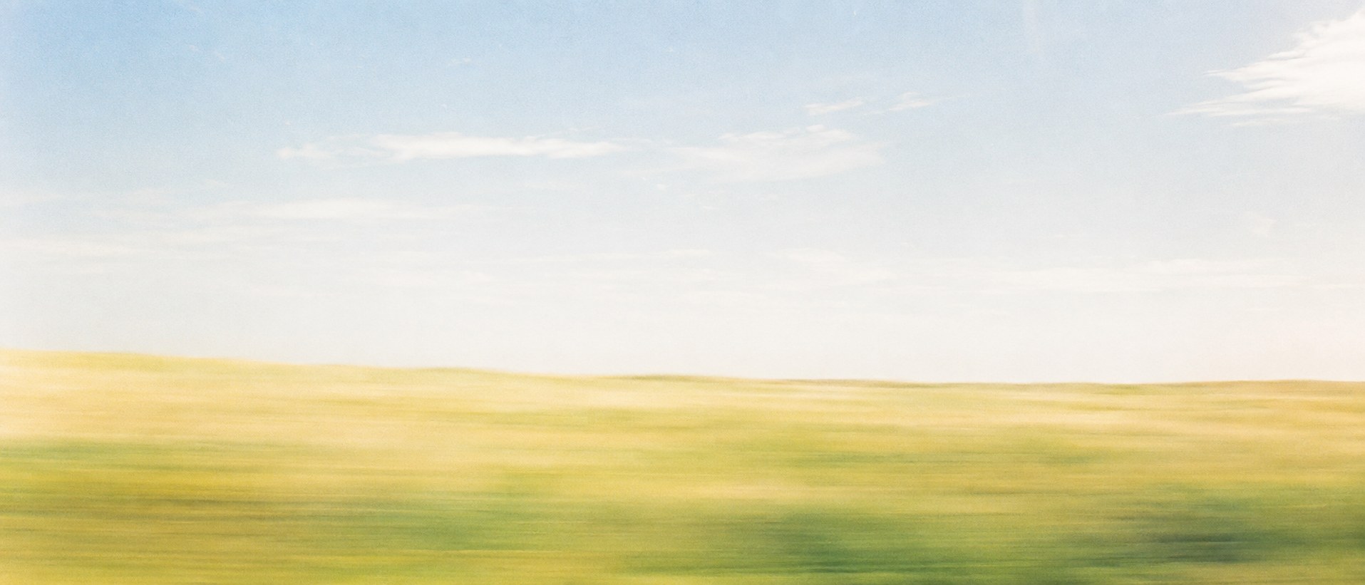 Bright open landscape seen from a moving train, blurred by motion