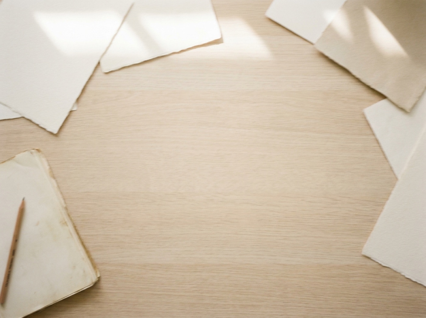 Loose sheets of paper and a notebook on a pale wooden desk